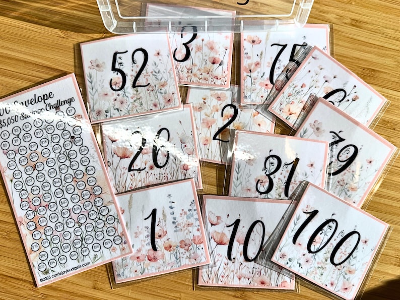 May include: A set of 10 floral-themed number cards, each with a different number from 1 to 100. The cards are printed on white cardstock with a pink and white floral design. The numbers are written in black ink.