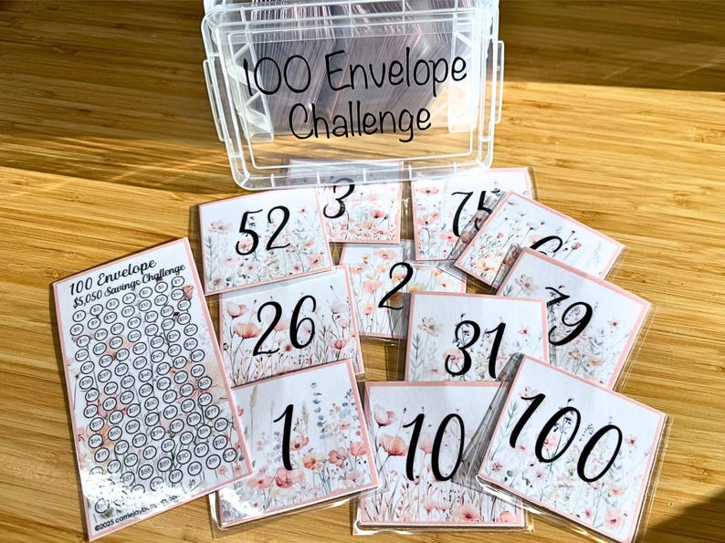 May include: A clear plastic container with the text "100 Envelope Challenge" on the lid.  The container holds small envelopes with numbers printed on them.  The numbers range from 1 to 100.  There is also a sheet of paper with a grid of 100 circles, each with a number inside.