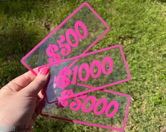 May include: Three clear plastic cards with pink borders and pink dollar amounts printed on them. The cards read "$500", "$1000", and "$5000".