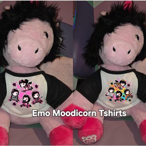 May include: A plush unicorn toy with black hair and pink hooves wearing a raglan t-shirt with black sleeves and a white body. The shirt features cartoon unicorn graphics and the text "NOT A PHASE" and "Emo Moodicorn Tshirts".