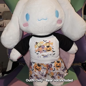 May include: A white plush toy wearing a Halloween-themed outfit. The outfit includes a white and black raglan shirt with cartoon characters and a pair of shorts with pumpkin and character prints. The text on the image reads "Outfit Only - Bear not included."