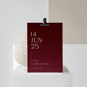 May include: A burgundy save the date card with white text. The card reads "14 JUN 25" and "save the date for the wedding of CLAIRE & LOUIS formal invitation to follow".