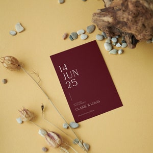May include: A burgundy save the date card with white text. The card reads "14 JUN 25" and "Save the date for the wedding of CLAIRE & LOUIS. Formal invitation to follow."