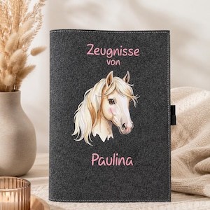 Könnte beinhalten: Dunkelgraue Filzhülle mit einer Pferdeillustration und dem Namen "Paulina" in Rosa. Die Hülle trägt den Text "Zeugnisse von" in Rosa. Die Pferdeillustration zeigt ein weißes Gesicht, eine hellbraune Mähne und rosa Akzente.