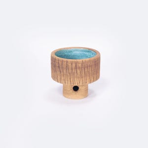 May include: A small, brown ceramic planter with a teal glaze inside. The planter has a textured, geometric pattern around the rim.