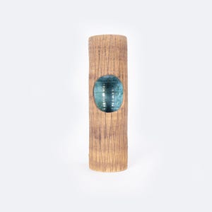 May include: A tall, brown ceramic vase with a textured surface and a circular opening revealing a blue-green interior.