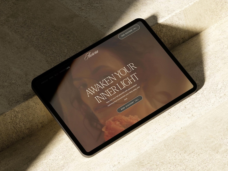 May include: A black tablet displays a website with the word "Aurora" at the top. The text "Awaken Your Inner Light" is prominently featured, along with a call to action button. The background has a warm, inviting color palette.