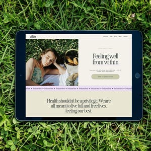 May include: A black tablet displaying a website with the text "Feeling well from within" and "Health shouldn't be a privilege." The tablet is set on a bed of green grass. The website features a photo of a person.