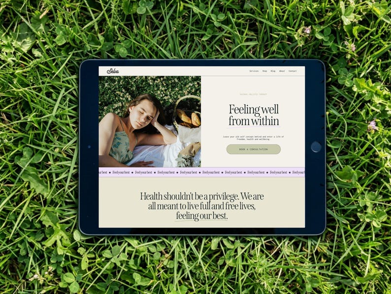 May include: A black tablet displaying a website with the text "Feeling well from within" and "Health shouldn't be a privilege." The tablet is set on a bed of green grass. The website features a photo of a person.