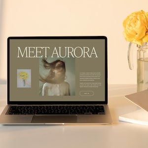 May include: A laptop displaying a website with the text "MEET AURORA" and a photo of a person with flowing hair. A bouquet of yellow flowers in a glass vase sits to the right, with a notebook and pen nearby. The scene is bathed in warm light.