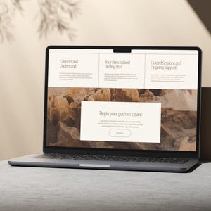 May include: A silver laptop displaying a website with the text "Connect and Understand", "Your Personalized Healing Plan", and "Guided Sessions and Ongoing Support". The website also features the text "Begin your path to peace". The laptop is on a gray surface.
