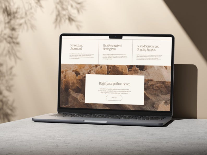 May include: A silver laptop displaying a website with the text "Connect and Understand", "Your Personalized Healing Plan", and "Guided Sessions and Ongoing Support". The website also features the text "Begin your path to peace". The laptop is on a gray surface.