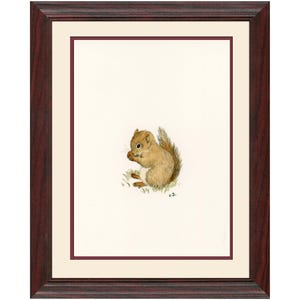 Op de afbeelding: Een ingelijste aquarelprint van een eekhoorn. De eekhoorn is afgebeeld in bruin- en beigetinten, zittend op een plukje groen gras, met een noot in zijn handen. De lijst is donkerroodbruin met een cr&egrave;mekleurige passe-partout.