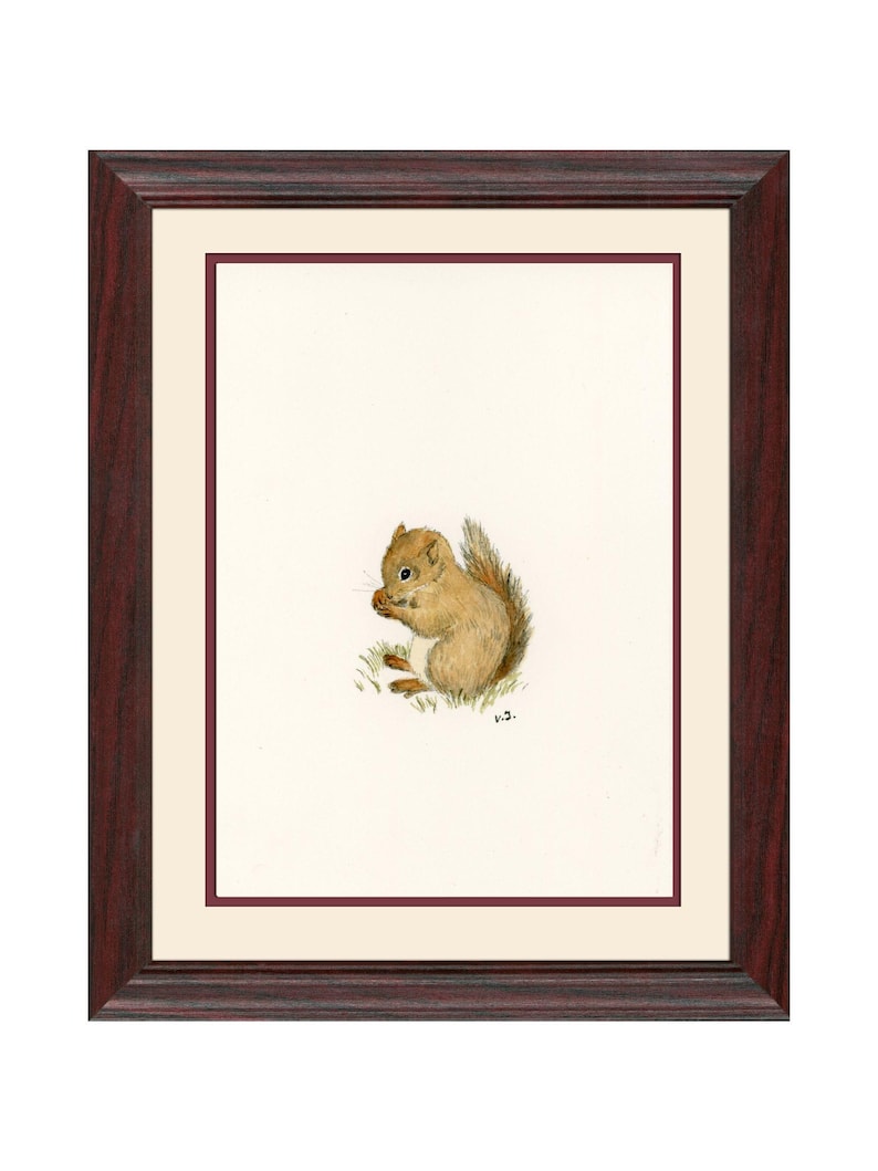 Op de afbeelding: Een ingelijste aquarelprint van een eekhoorn. De eekhoorn is afgebeeld in bruin- en beigetinten, zittend op een plukje groen gras, met een noot in zijn handen. De lijst is donkerroodbruin met een cr&egrave;mekleurige passe-partout.