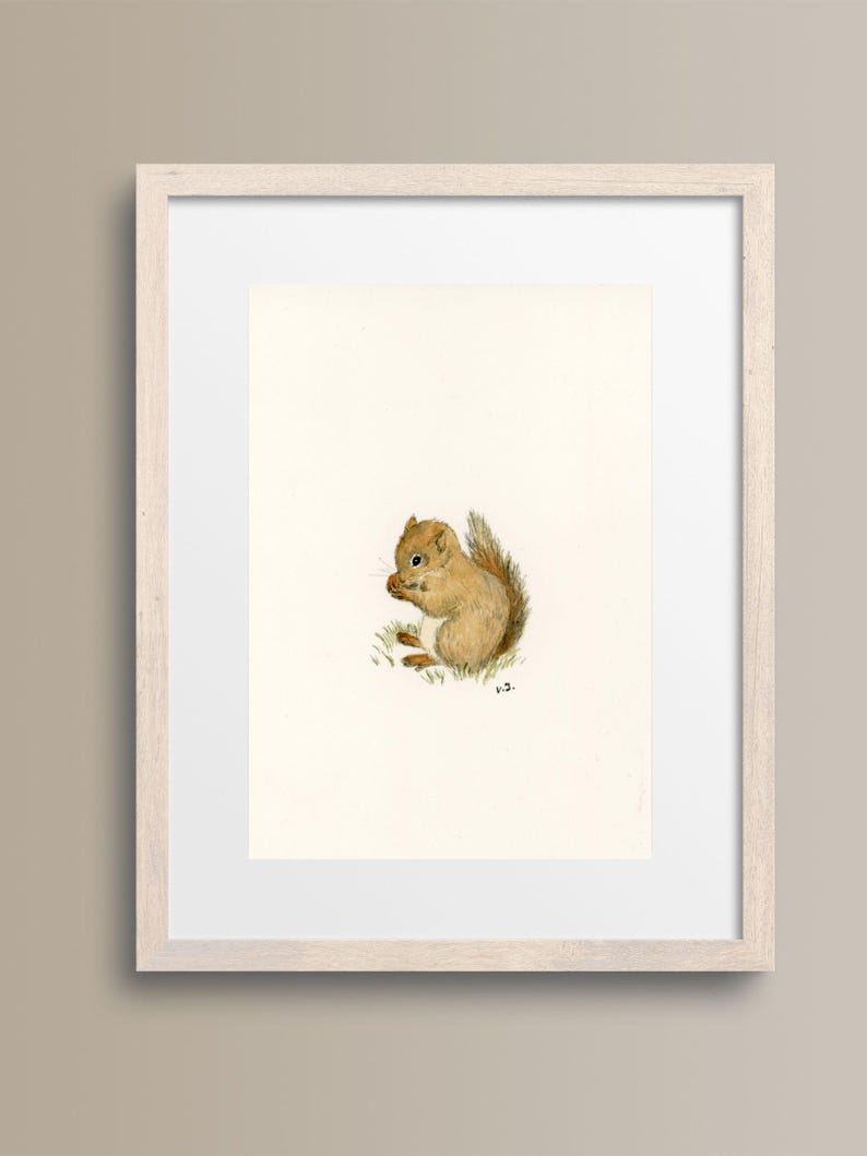 Op de afbeelding: Ingelijste aquarelprint van een eekhoorn. De eekhoorn is afgebeeld in een zittende positie, met een noot in zijn handen. Het kunstwerk staat tegen een witte achtergrond, met een lichtbeige lijst. De eekhoorn heeft bruine vacht en een pluizige staart.