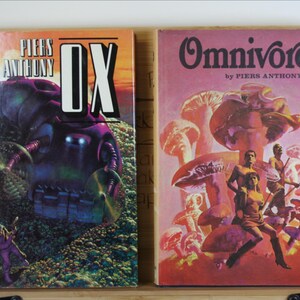 May include: Two vintage science fiction books. The first book, "OX" by Piers Anthony, features a purple robot on the cover. The second book, "Omnivore" by Piers Anthony, depicts figures among giant mushrooms, with a pink and orange color scheme.
