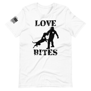 May include: White t-shirt with a black silhouette of a person and a dog with the text "LOVE BITES" printed on it. The silhouette of the dog is biting the person's arm. The person has a heart on their chest. The dog has a heart on its chest. The text is in a distressed font.