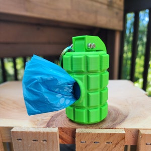 May include: A green plastic dog poop bag dispenser shaped like a grenade. The dispenser has a blue plastic bag hanging out of the top.