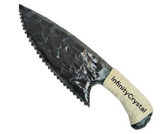 May include: A black obsidian knife with a serrated edge and a wrapped handle. The handle is wrapped with a cream-colored material and features the text "Infinity Crystal". The knife is designed with a curved blade.