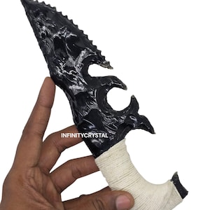 May include: A black obsidian dagger with a serrated blade and a wrapped handle. The handle is wrapped with white twine. The text "INFINITYCRYSTAL" is visible on the handle.