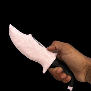 May include: A pink and white stone knife with a black wrapped handle. The knife has a curved blade and is held in a hand against a black background. The text "InfinityCrystal" is visible on the blade.