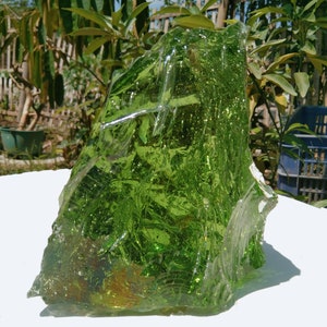 May include: A large, green, glass rock with a rough, textured surface. The rock is translucent and has a slight shimmer.
