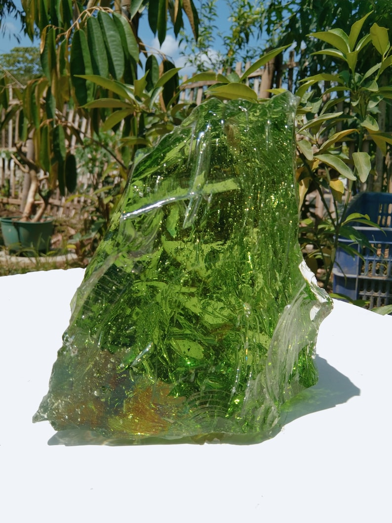 May include: A large, green, glass rock with a rough, textured surface. The rock is translucent and has a slight shimmer.