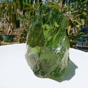May include: A large, green, glass rock with a rough, textured surface. The rock is translucent and has a slightly iridescent sheen.