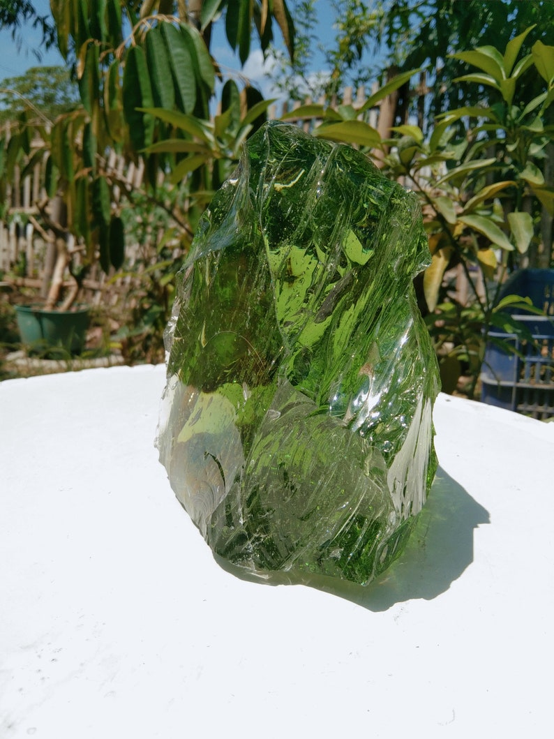 May include: A large, green, glass rock with a rough, textured surface. The rock is translucent and has a slightly iridescent sheen.