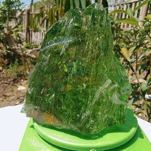 May include: A large, green, translucent piece of glass with a rough, irregular shape. The glass is sitting on a green scale.