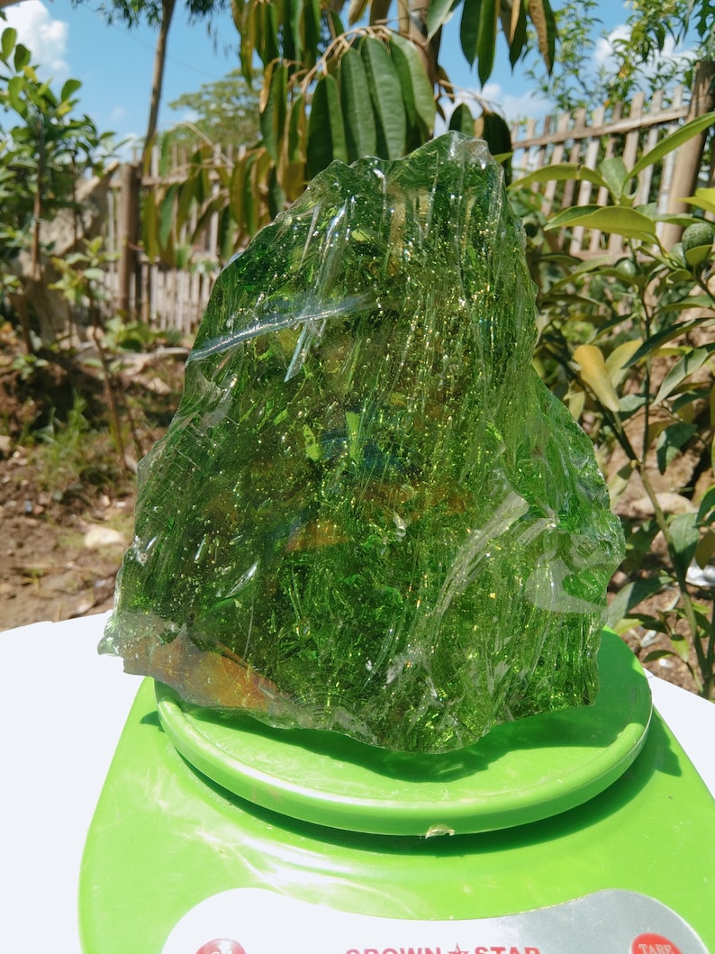May include: A large, green, translucent piece of glass with a rough, irregular shape. The glass is sitting on a green scale.