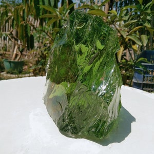 May include: A large, irregularly shaped piece of green glass. The glass is translucent and has a rough, textured surface.