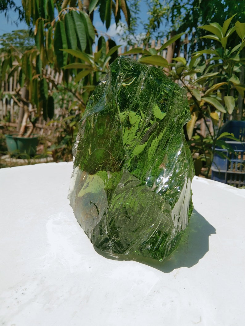 May include: A large, irregularly shaped piece of green glass. The glass is translucent and has a rough, textured surface.
