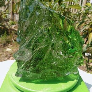 May include: A large, irregularly shaped piece of green glass, likely a piece of sea glass, on a green platform.