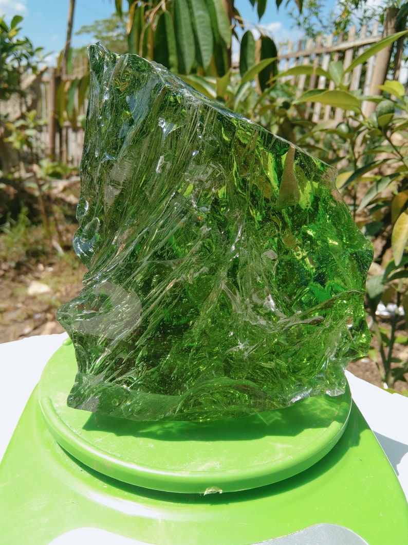 May include: A large, irregularly shaped piece of green glass, likely a piece of sea glass, on a green platform.
