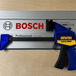Puede incluir: Una abrazadera azul Irwin Quick-Grip unida a una sierra de riel Bosch Professional FSN 1600 plateada. La abrazadera tiene un mango negro y una etiqueta amarilla con el logotipo de Irwin Quick-Grip.