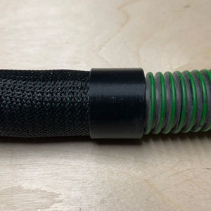 Puede incluir: Un conector de manguera negro con una manguera trenzada negra a un lado y una manguera corrugada verde al otro.