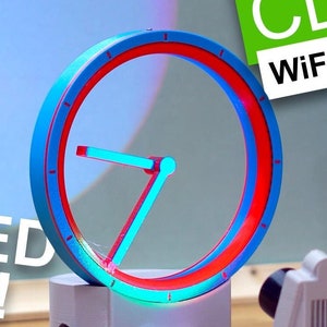 May include: A 3D printed clock with a blue and red ring. The clock projects a shadow of the time onto a wall. The text "HOW TO BUILD A SHADOW CLOCK WiFi - 3D Printed" is visible in the background.