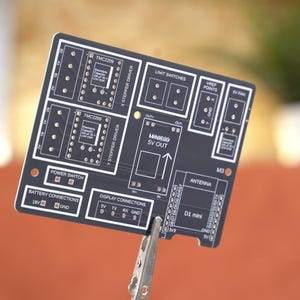 May include: A black rectangular printed circuit board featuring white silkscreen labels including TMC2209, X STEPPER DRIVER, Y STEPPER DRIVER, LIMIT SWITCHES, VREF POINTS, 5V FAN, POWER SWITCH, BATTERY CONNECTIONS 18V, DISPLAY CONNECTIONS, and D1 mini.
