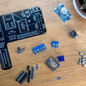 May include: An assortment of electronic components, including a black circuit board with white text reading "DIYMACHINES.CO.UK", blue and black circuit boards, and various connectors and screws. The components are arranged on a wooden surface.