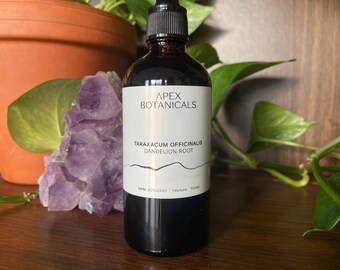 May include: A dark brown glass bottle with a dropper top, labelled "Apex Botanicals Taraxacum Officinalis Dandelion Root" with a white label and black text. The bottle is sitting on a wooden surface.