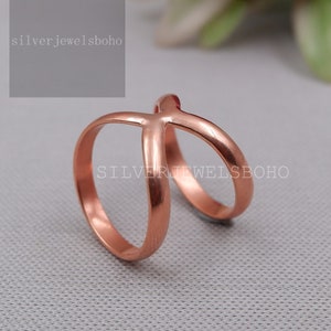 May include: A rose gold colored ring with a criss-cross design. The ring is made of metal and has a polished finish.  The ring is a simple and elegant design that would be perfect for everyday wear.