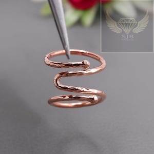 May include: A rose gold hammered metal ring with a spiral design. The ring is made of two intertwined bands.