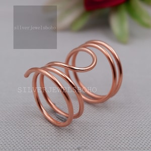 May include: A rose gold colored, triple-wrapped wire ring. The ring is made of a single piece of wire that is twisted and shaped into a ring. The wire is smooth and shiny.