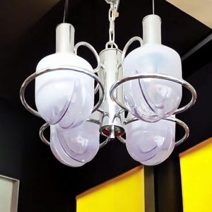 Peut inclure: Un lustre en chrome et verre avec cinq abat-jours en verre givré. Les abat-jours ont une texture ondulée et sont maintenus en place par des anneaux chromés.