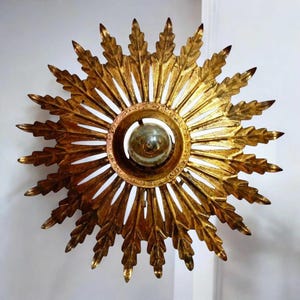 May include: A gold metal sunburst ceiling light fixture with a round, open center and a light bulb inside. The fixture has a decorative, leaf-like design.