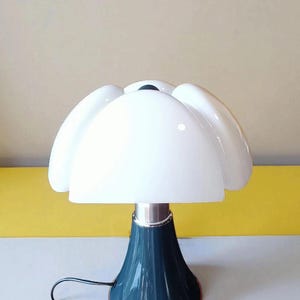 Puede incluir: Lámpara de mesa blanca con forma de pétalo, con base azul oscuro y tallo plateado. La lámpara tiene un acabado brillante y un cable de alimentación negro. El diseño es moderno y elegante.