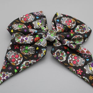 May include: A black bow with a colourful sugar skull pattern. The bow is made of fabric and has a pointed shape.