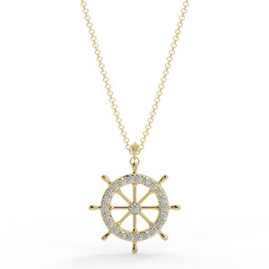 May include: A gold-colored necklace featuring a ship's wheel pendant. The wheel is encrusted with small, clear gemstones around the outer rim. The necklace has a delicate chain and a simple clasp.