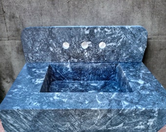 Puede incluir: Un lavabo de mármol azul con un salpicadero y tres agujeros para grifos. El lavabo está hecho de piedra natural y tiene un aspecto rústico.